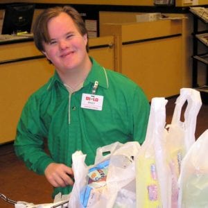 Smiling young adult with intellectual disabilities bags groceries at his new job at BiLo.