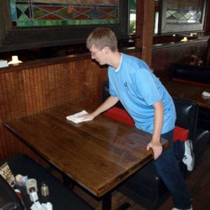 Young adult with intellectual disabilities cleans tables at his new job.